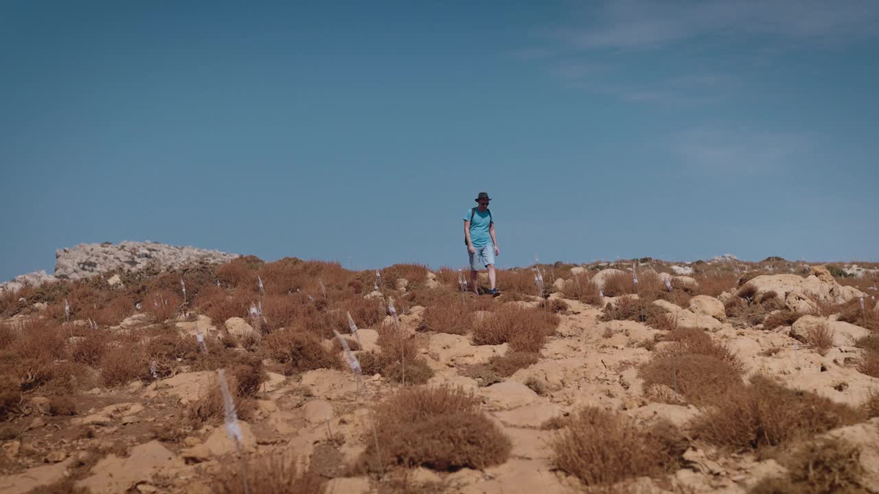 一个男人穿过长满灌木丛的小山。地中海的夏季和炎热视频素材