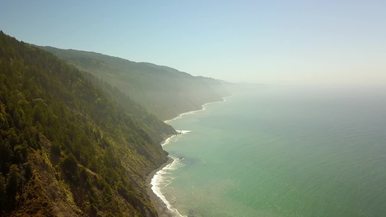 空中摇摄拍摄的海浪冲击海岸线对天空，无人机飞行在风景秀丽的山脉在阳光明媚的日子-北加州，加利福尼亚州视频素材