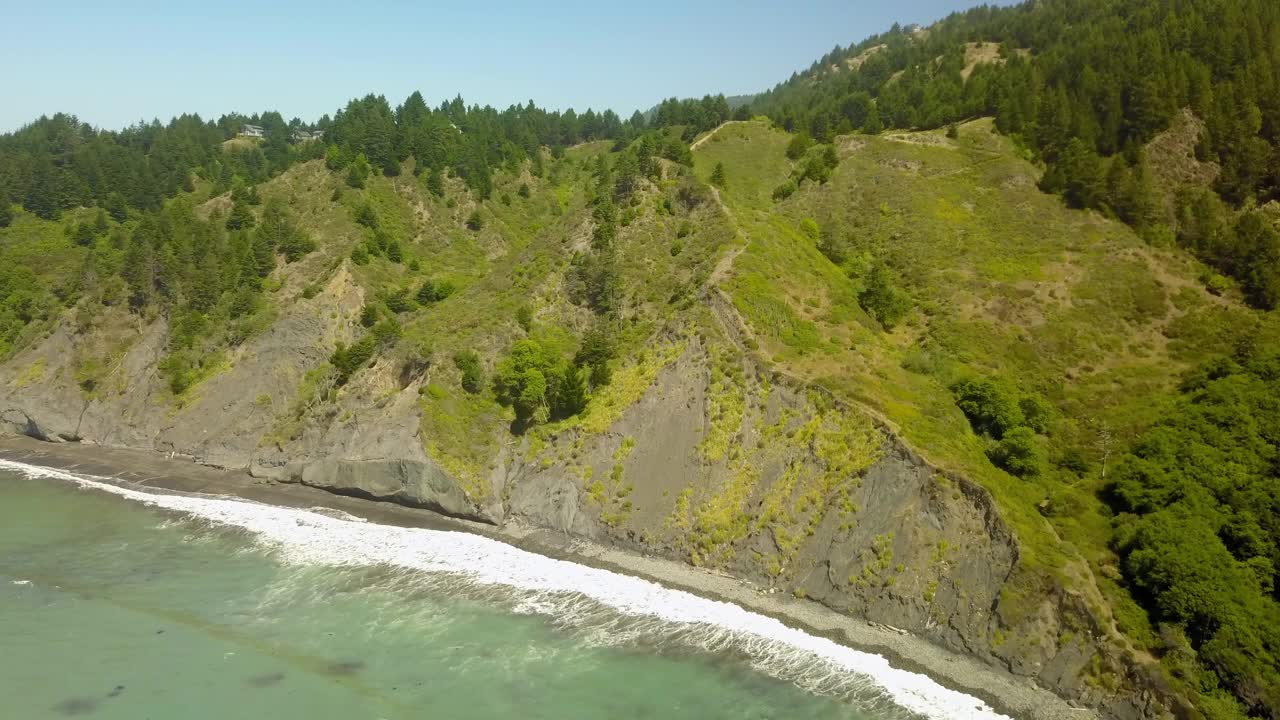 高空拍摄的海浪冲击悬崖在阳光明媚的日子，无人机飞行在绿色的树木在山上-北加州，加利福尼亚州视频素材