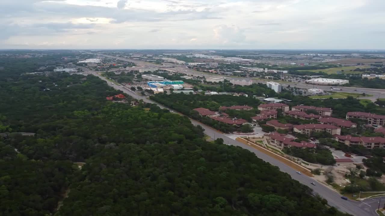 空中平移拍摄的车辆在道路上的住宅建筑在城市，无人机飞行在绿色的树木对多云的天空-奥斯汀，德克萨斯州视频素材