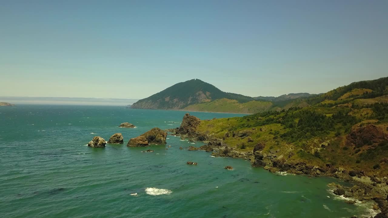 航拍的海浪冲击海岸线对蓝天，无人机上升在阳光明媚的日子海洋-俄勒冈海岸，俄勒冈视频素材