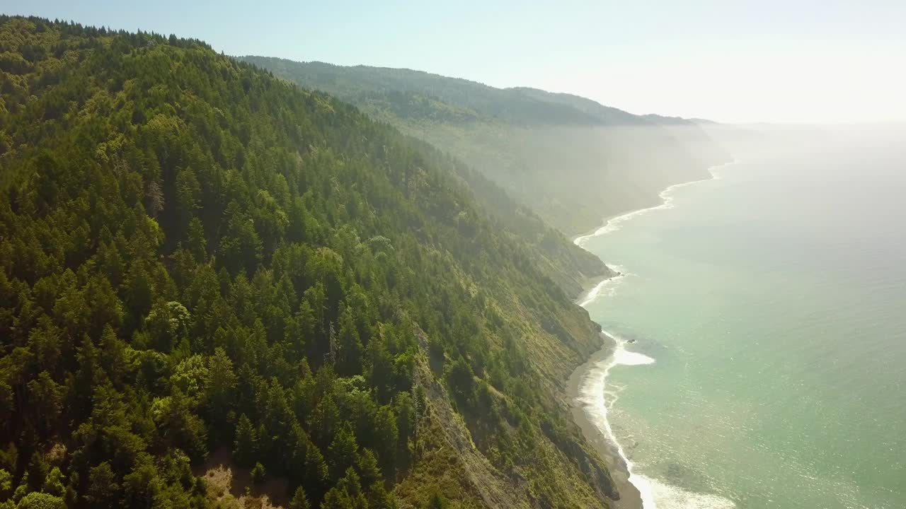 空中摇摄拍摄的海浪冲击海岸线在阳光明媚的日子，无人机飞行在风景秀丽的山脉由海对天-加利福尼亚北部视频素材