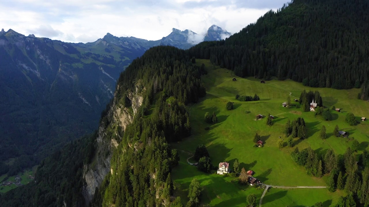 空中前进的美丽镜头的房子在绿色的山对多云的天空- Lauterbrunnen，瑞士视频素材