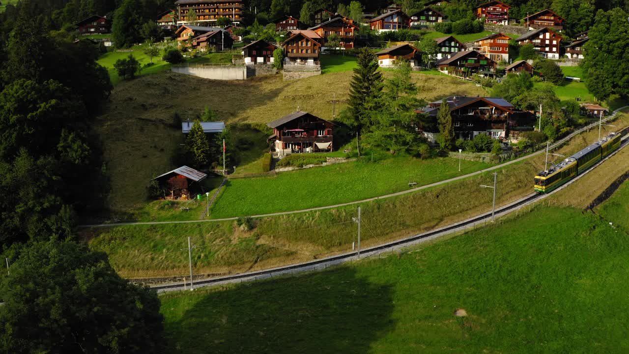 空中平移火车在轨道上移动的美丽镜头，无人机飞过村庄的树木- Lauterbrunnen，瑞士视频素材