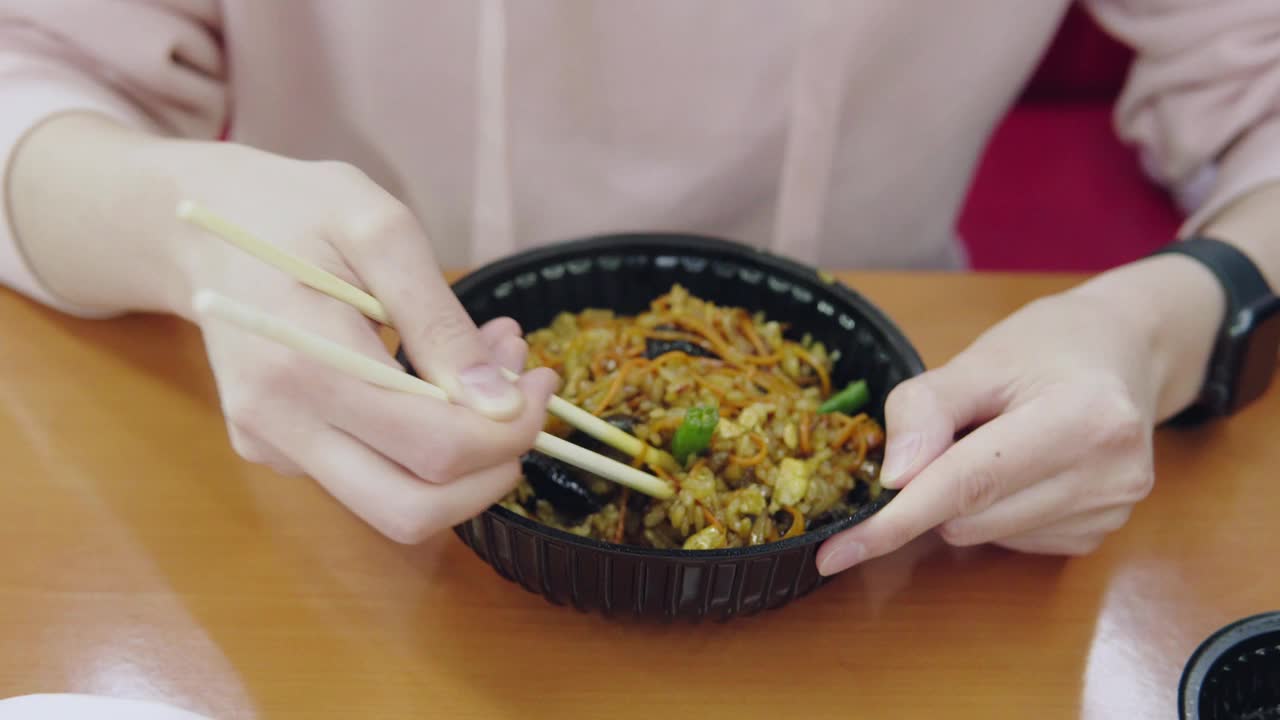 一位妇女坐在快餐店里吃面条，面条里有肉、蔬菜和酱料视频素材