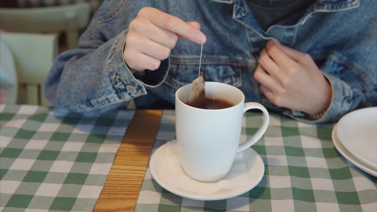 一个穿着牛仔夹克的女孩把一个茶包浸泡在一杯沸水里，泡茶视频素材