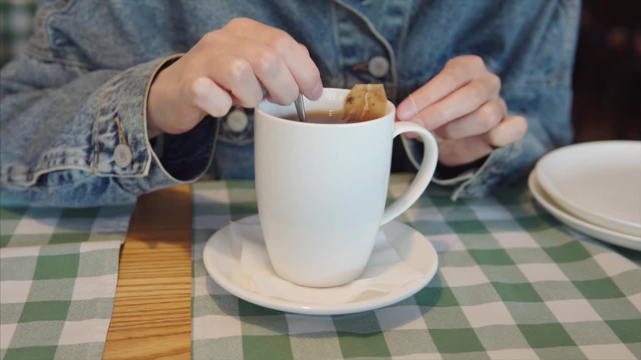 在一杯热茶中搅拌糖、甜叶菊或蜂蜜的女学生视频素材