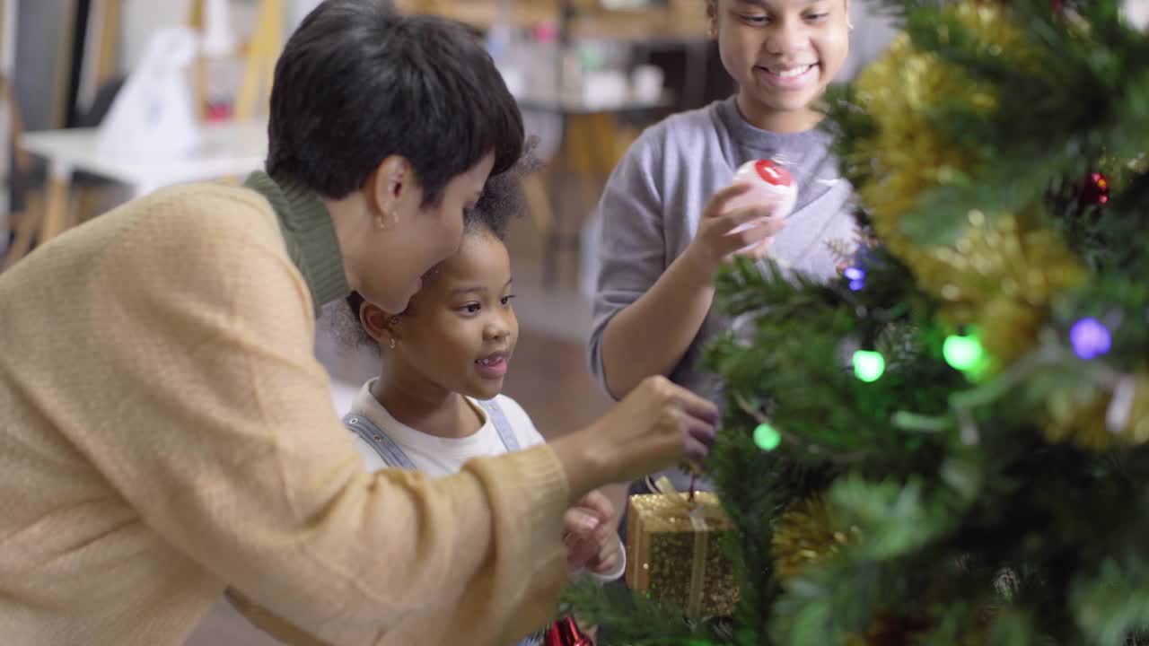 快乐的非洲裔美国女孩喜欢和她的父亲和亚洲母亲在家里庆祝传统节日文化装饰圣诞树视频素材