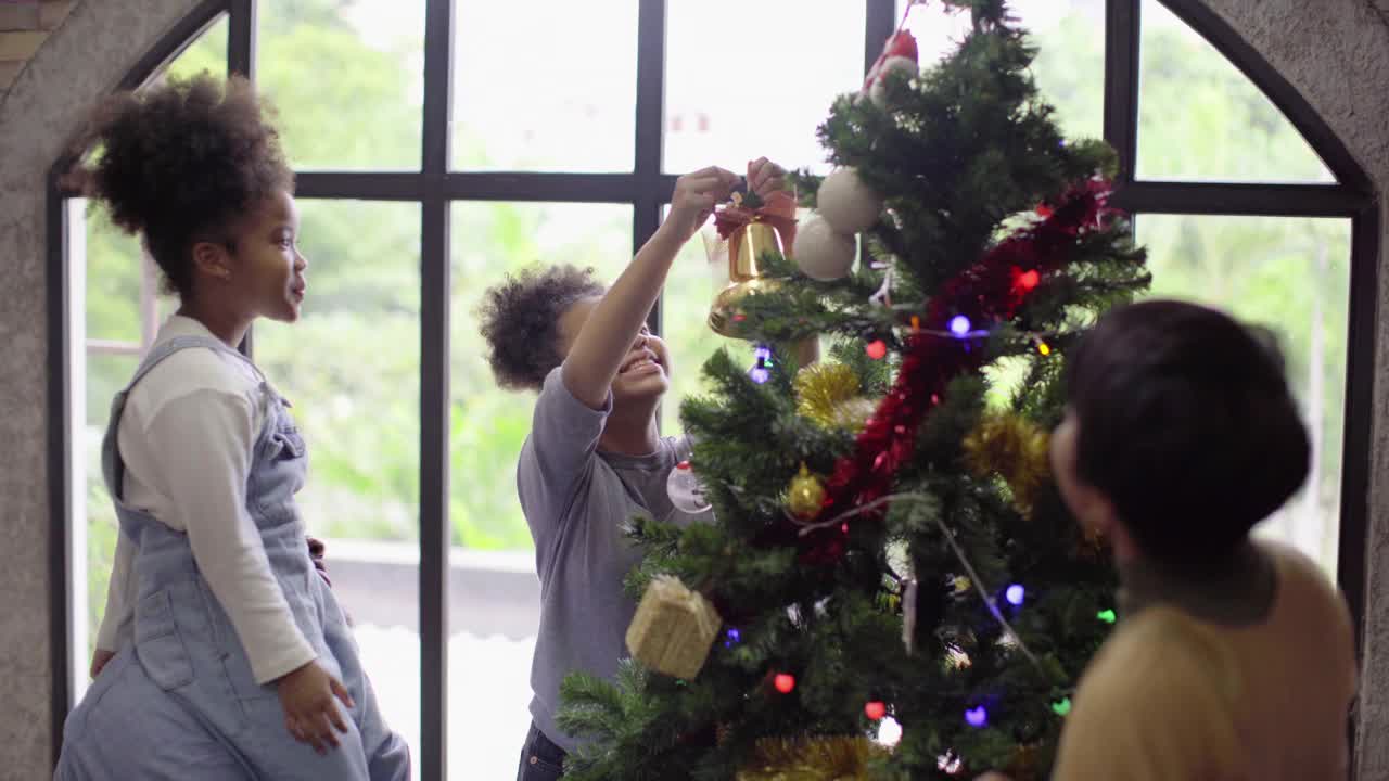 快乐的非洲裔美国女孩喜欢和她的父亲和亚洲母亲在家里庆祝传统节日文化装饰圣诞树视频素材