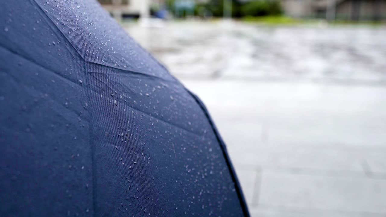 在下雨天，贴近伞上的水滴。实验对象在左边。背景是道路和汽车。视频素材