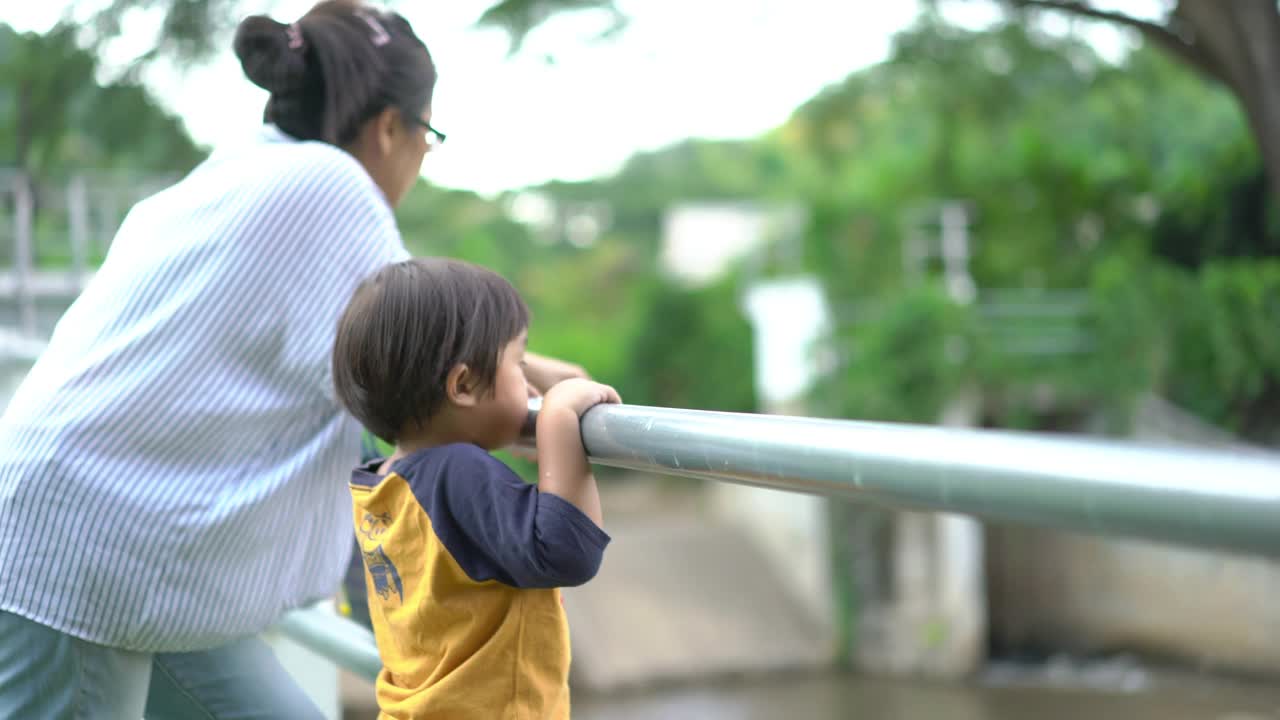 一个小男孩和妈妈站在河边，想看到一个堤坝视频素材