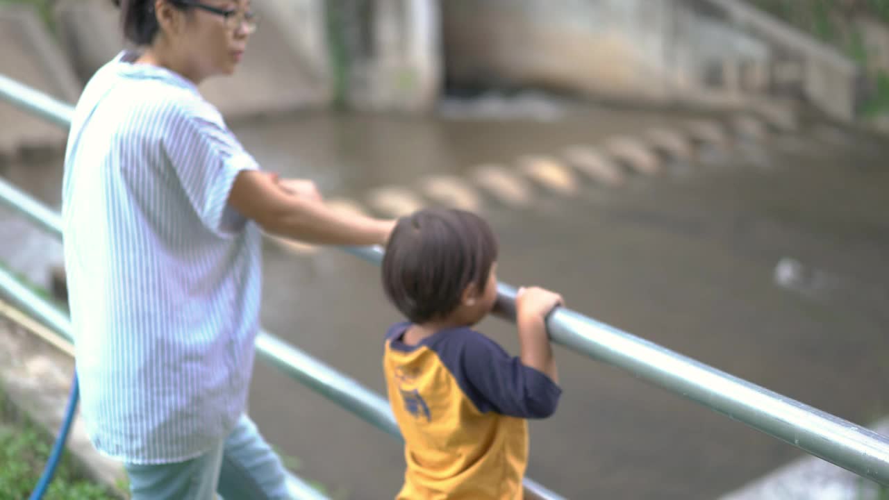 一个小男孩和妈妈站在河边，想看到一个堤坝视频素材