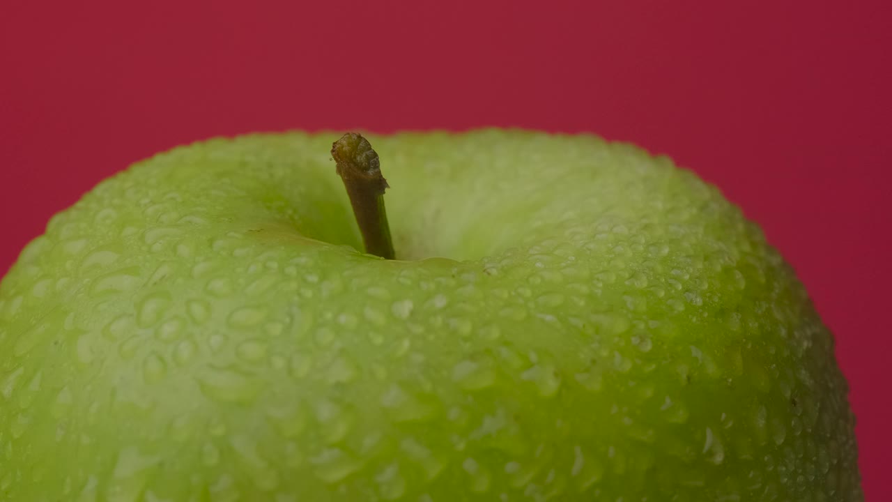 绿色湿苹果旋转挂在红色背景，孤立视频下载