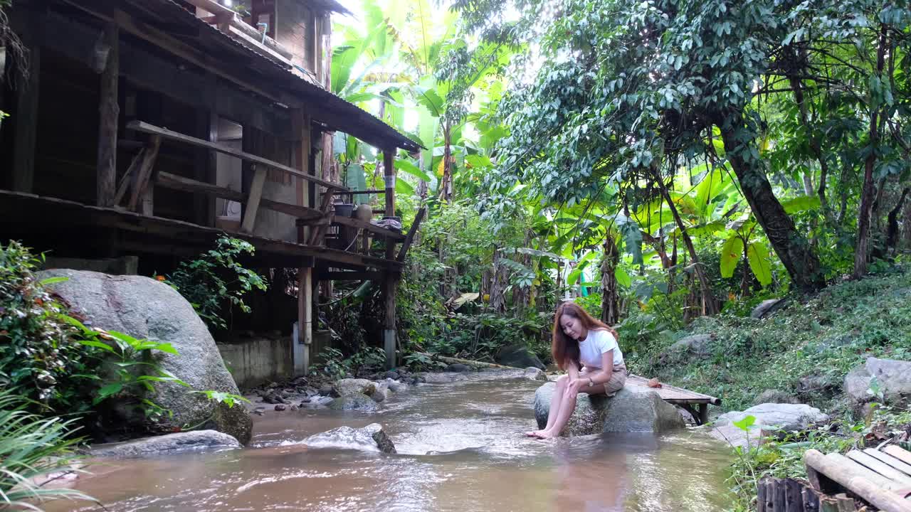 一个女人坐在森林里与瀑布溪流嬉戏视频素材