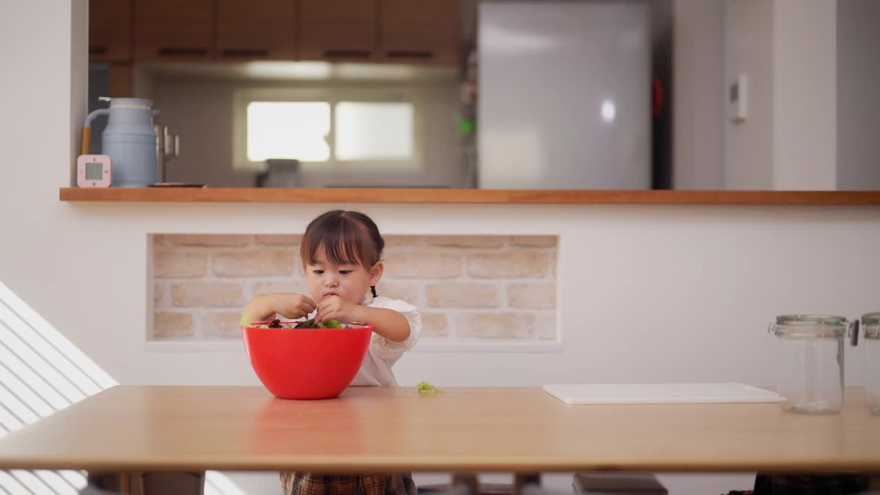 母亲和她的小女儿在家里准备沙拉。妈妈帮她的小女儿准备蔬菜，鼓励她健康饮食视频素材