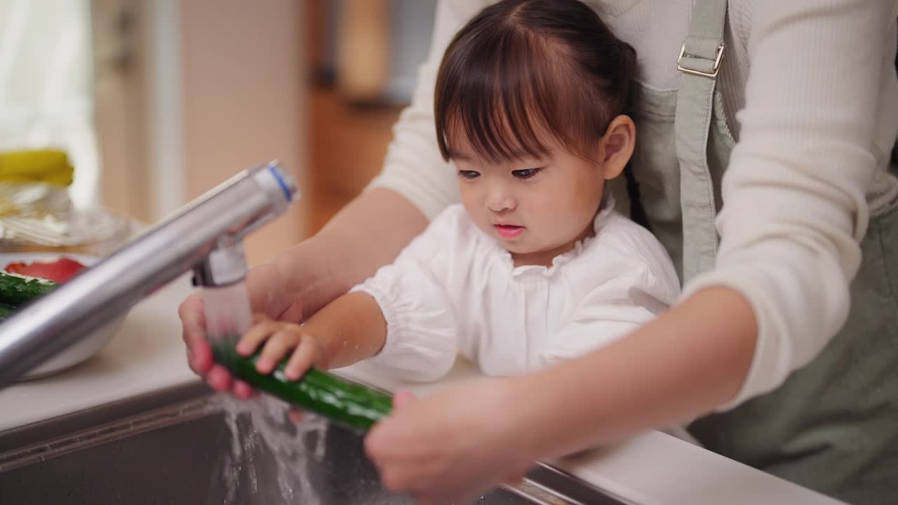 妈妈帮她的小女儿洗蔬菜，鼓励她健康饮食视频素材