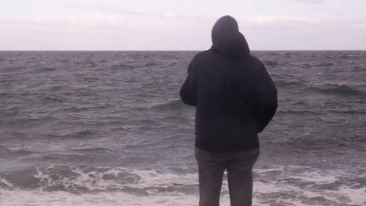 一个人站在海边，在一个暴风雨的秋日看着波涛汹涌的大海。视频下载