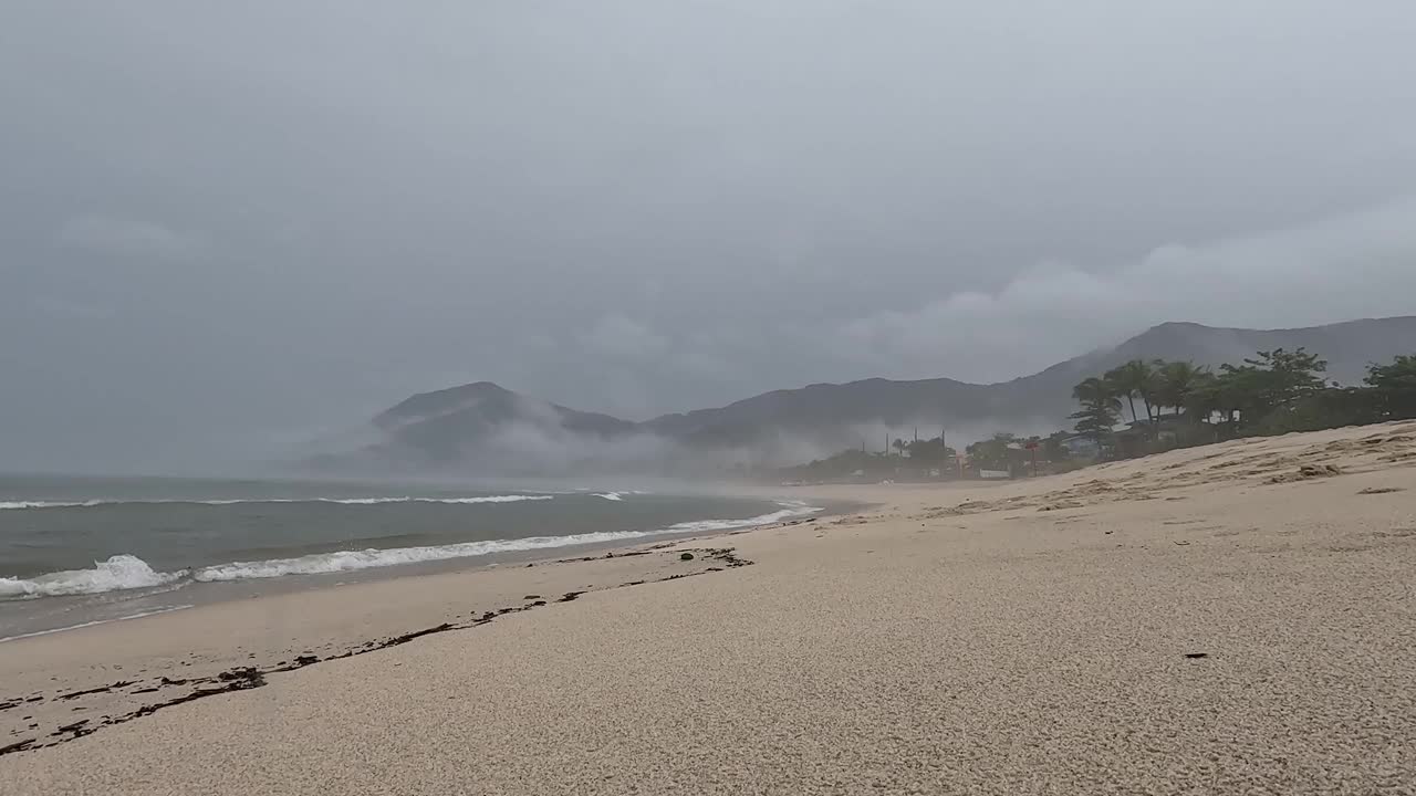 下雨天，与一个打着黄色伞的年轻女子在海边散步。视频素材