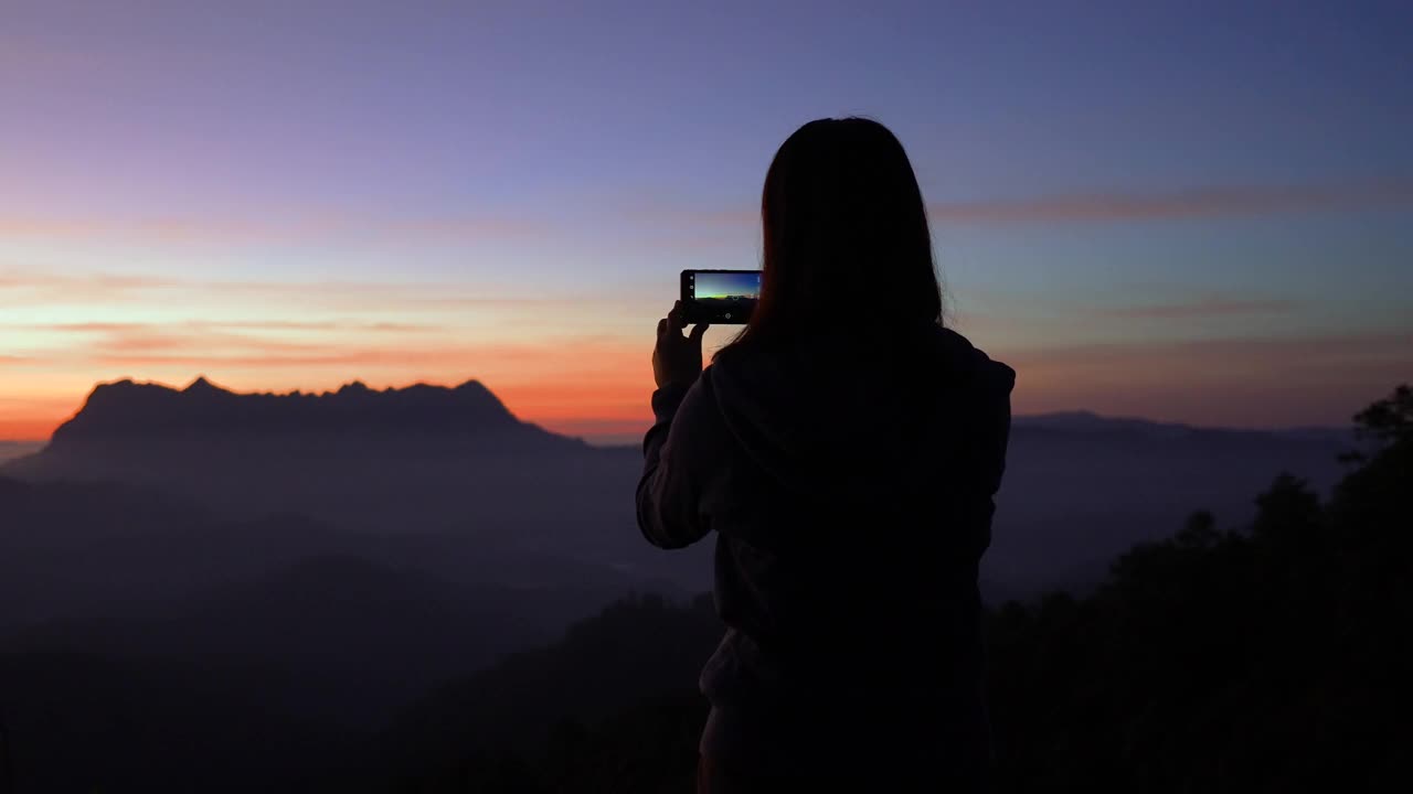 女旅行者在日出的时候在山上拍摄一个美妙的地方视频素材