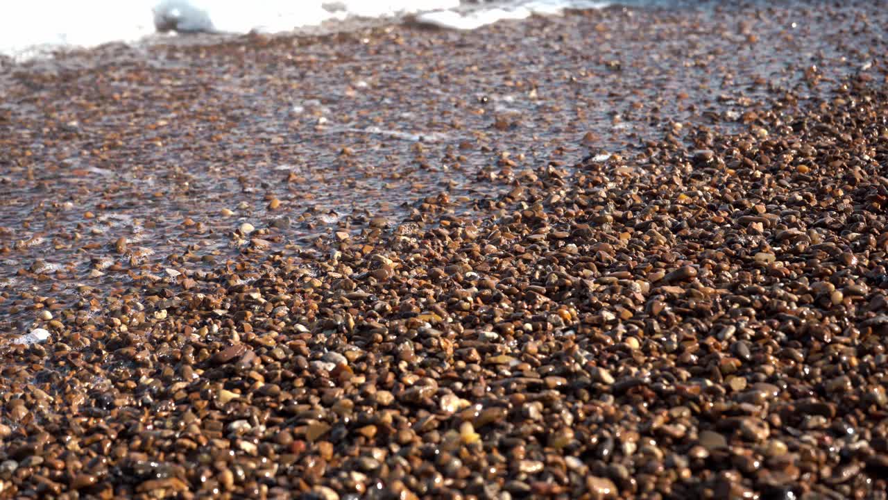 海浪拍打着大海的泡沫和闪亮光滑的鹅卵石。海浪冒着泡沫，淹没了卵石滩。视频素材