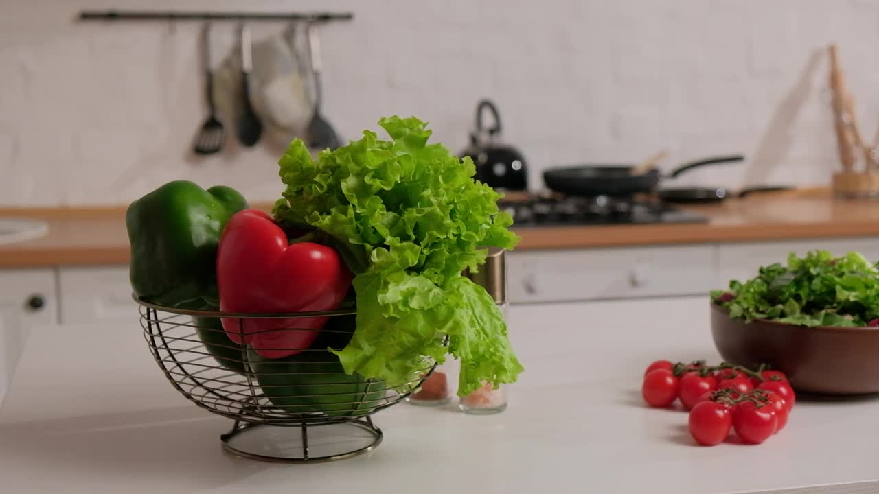 新鲜的蔬菜沙拉，绿色和红色的辣椒和樱桃西红柿摆在桌子上，背景是白色的厨房视频素材