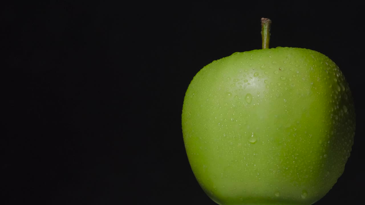 绿色的湿苹果旋转挂在黑暗的背景，孤立视频下载