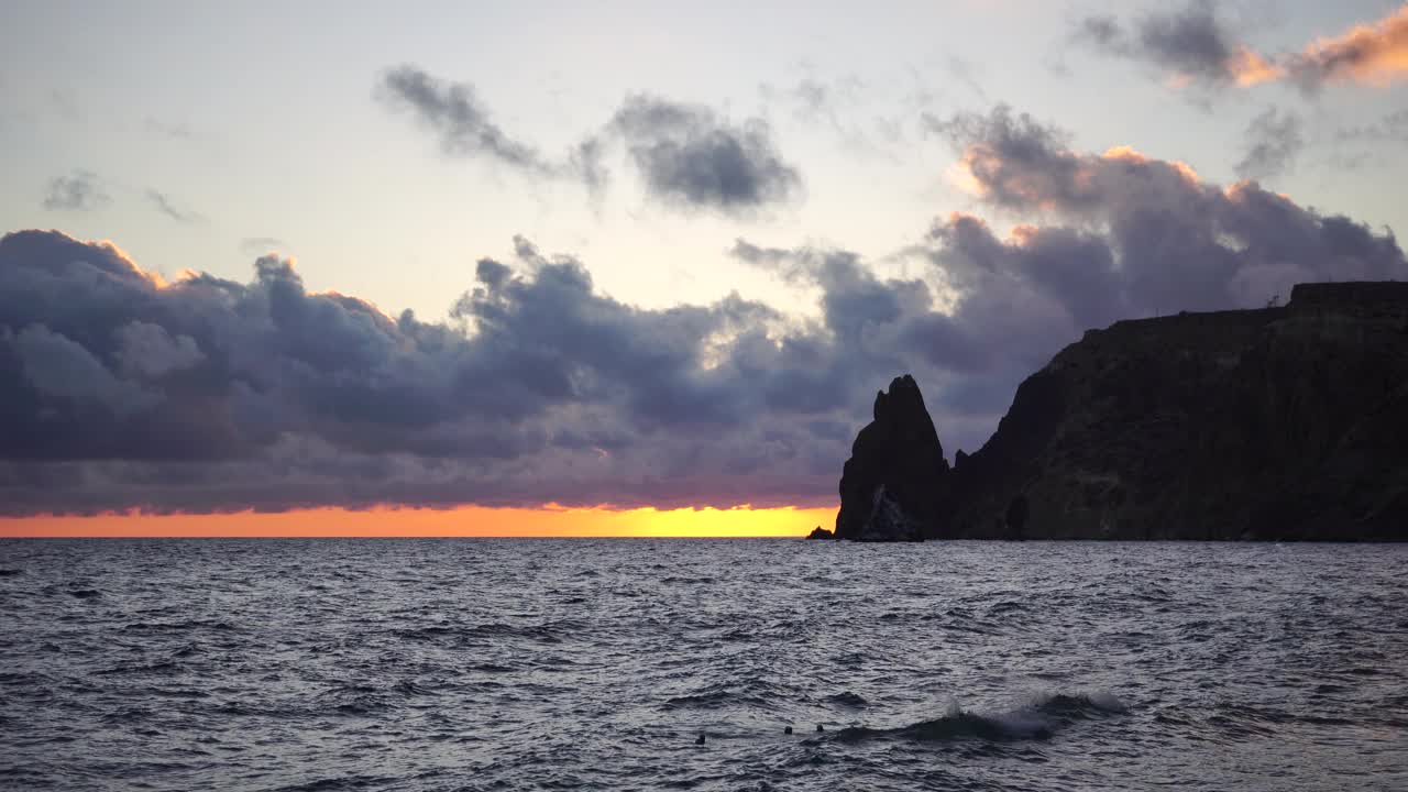 多彩的温暖的日落在海上和火山玄武岩，就像在冰岛。海浪冲击着岩石，在温暖的落日的照耀下，浪花飞溅，浪花翻滚。永恒的自然之美视频素材