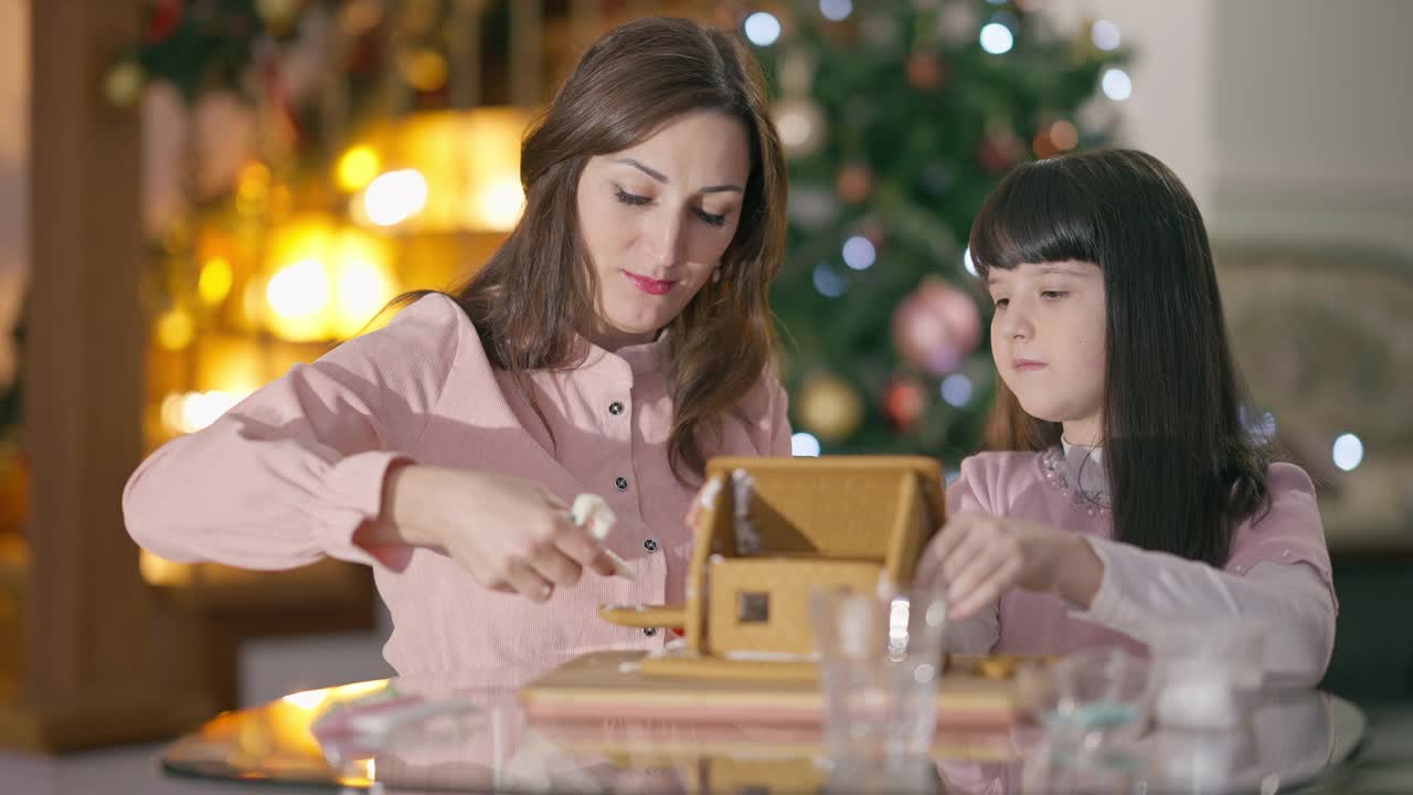 除夕之夜，年轻女子和女孩在家里用食用糖胶聚姜房子。无忧无虑的白人母亲和女儿在圣诞节烹饪美味的传统甜点视频素材