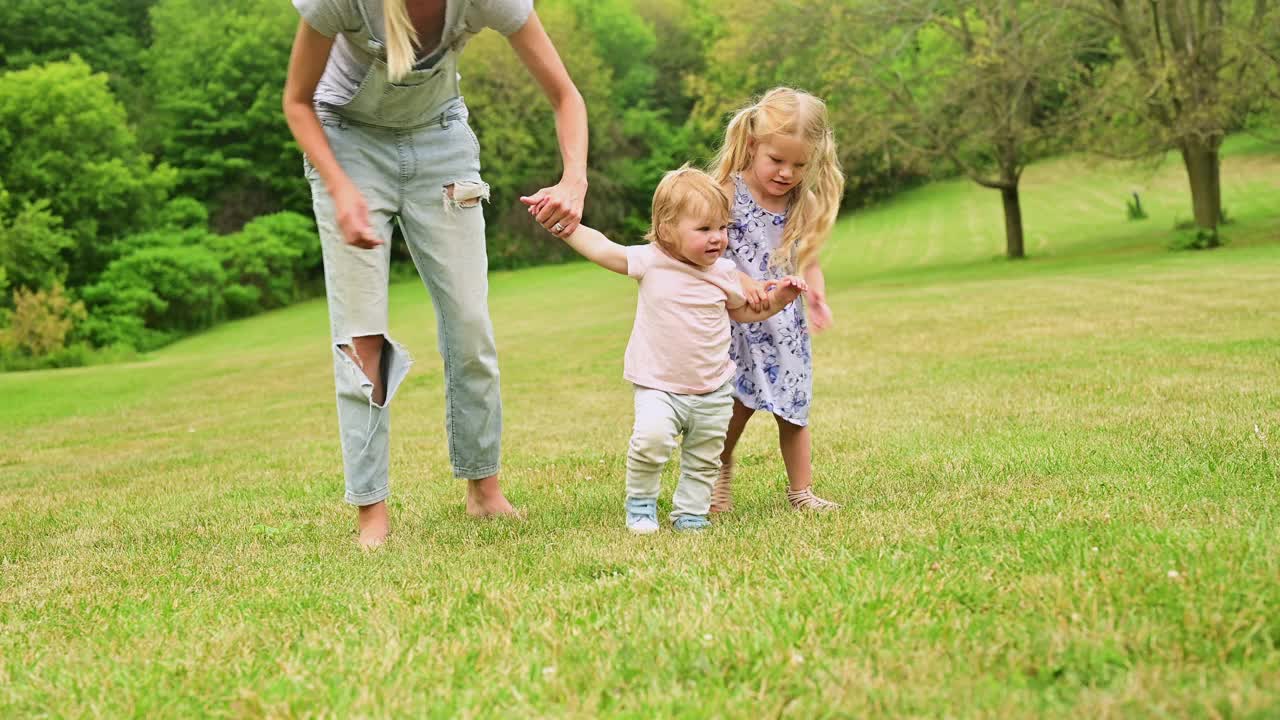 母亲和年幼的女儿牵着蹒跚学步的孩子的手。视频素材