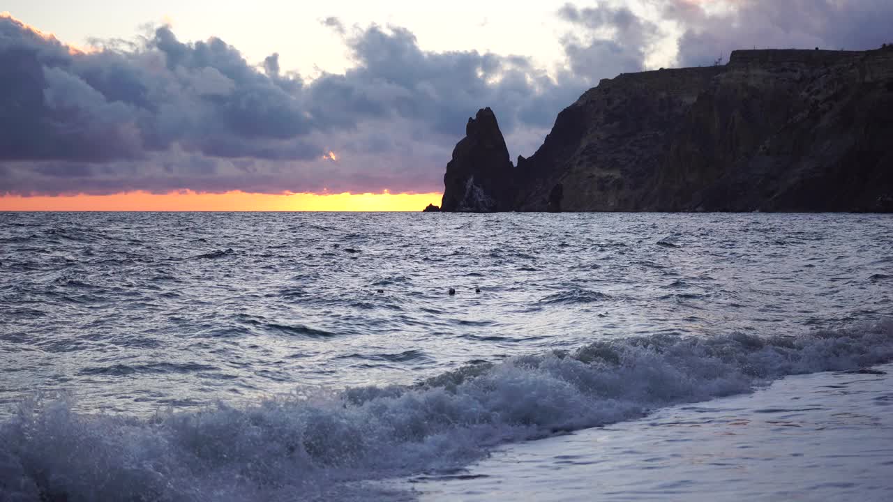 多彩的温暖的日落在海上和火山玄武岩，就像在冰岛。海浪冲击着岩石，在温暖的落日的照耀下，浪花飞溅，浪花翻滚。永恒的自然之美视频素材