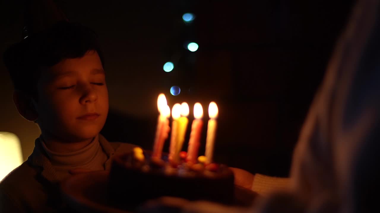 可爱的小男孩享受吹蜡烛生日蛋糕在黑暗的房间里用散焦灯庆祝。视频素材