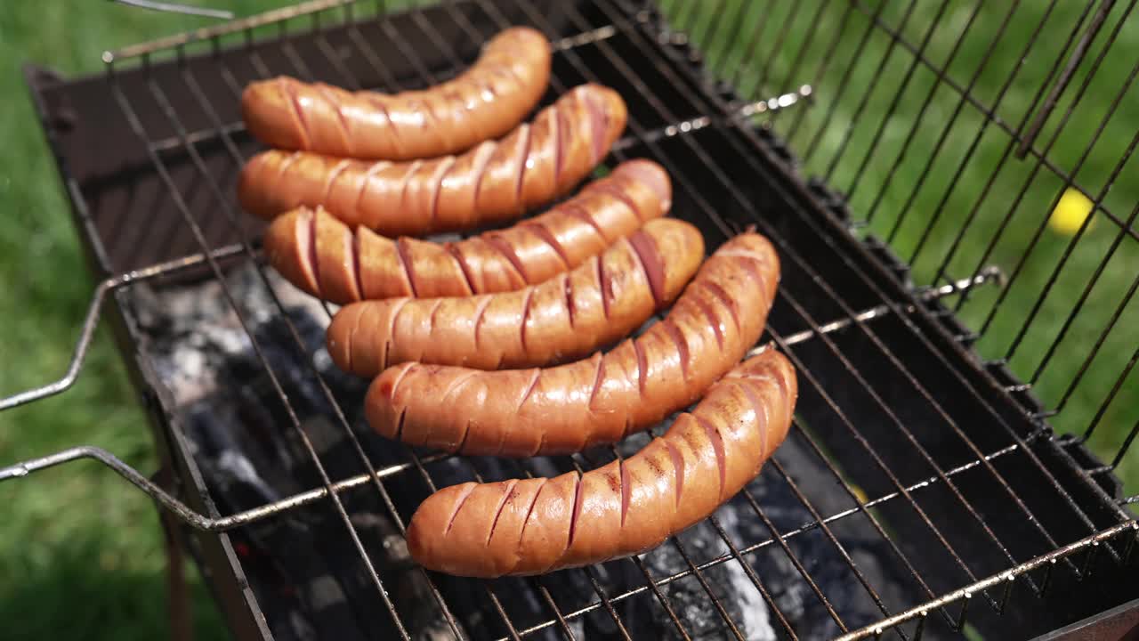 在木炭烧烤架上烤腊肠。夏天，厨师在花园里用食物钳烤着热香肠。野餐的美味食物。视频素材