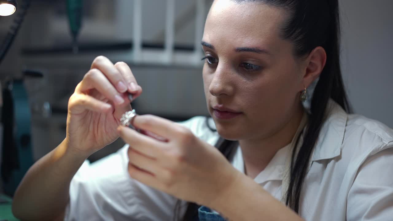 年轻专注的女珠宝商在戒指上用慢动作雕刻宝石。肖像集中技术熟练的专业白人妇女创造手工银配件在车间。视频素材