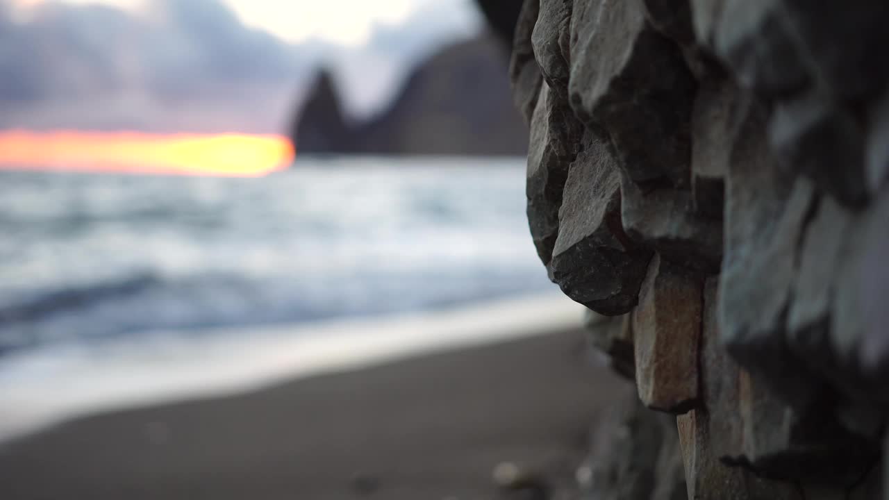 多彩的温暖的日落在海上和火山玄武岩，就像在冰岛。海浪冲击着岩石，在温暖的落日的照耀下，浪花飞溅，浪花翻滚。永恒的自然之美视频素材