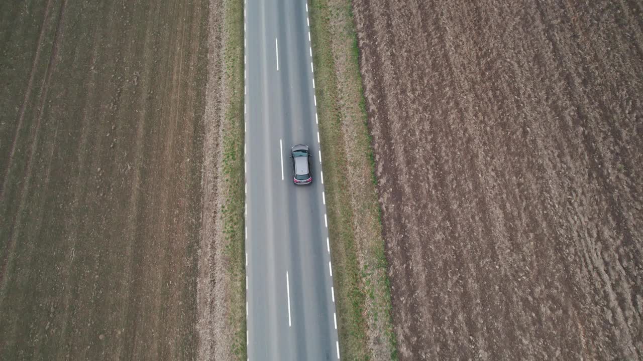 这辆车正行驶在穿过田野的道路上，无人机拍摄了航拍画面。秋天的时候在柏油路上，摄影机跟在车的后面。视频素材