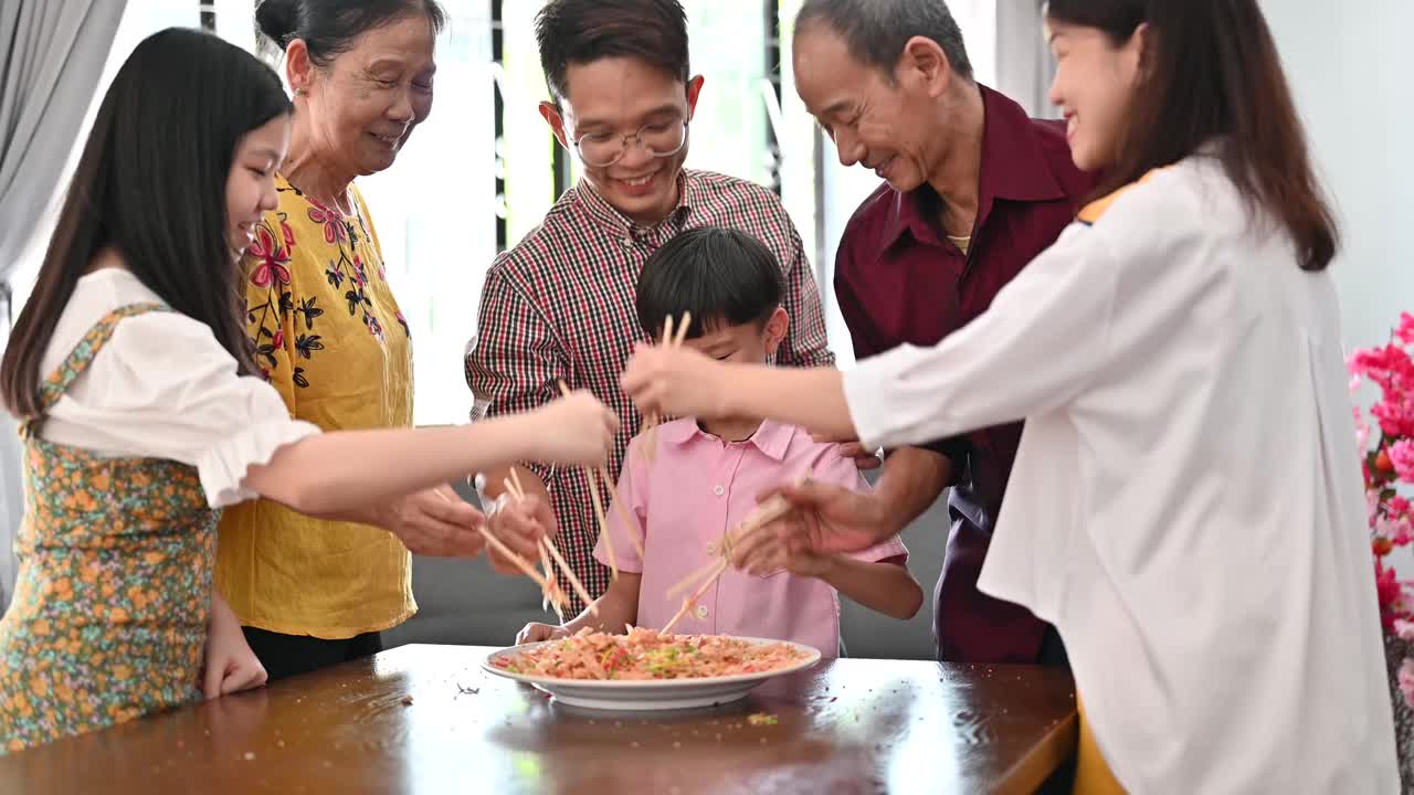 一个亚洲家庭在团圆饭上用传统食物“生鱼”庆祝中国新年视频素材