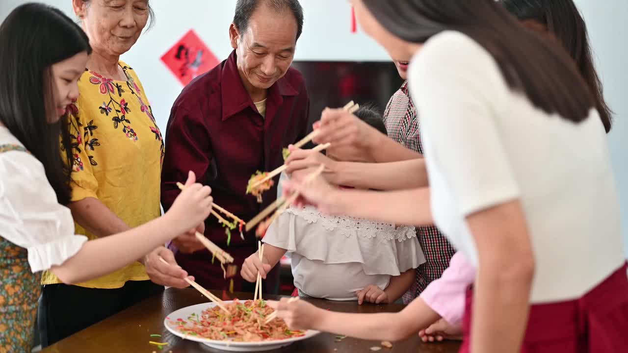 一个亚洲家庭在团圆饭期间用传统食物“生鱼”庆祝中国新年视频素材