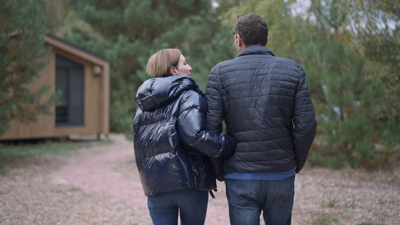 现场镜头跟随幸福相爱的白人夫妇在户外牵着手散步。成年男女笑着聊天，走在后院。关系和幸福的概念。视频素材