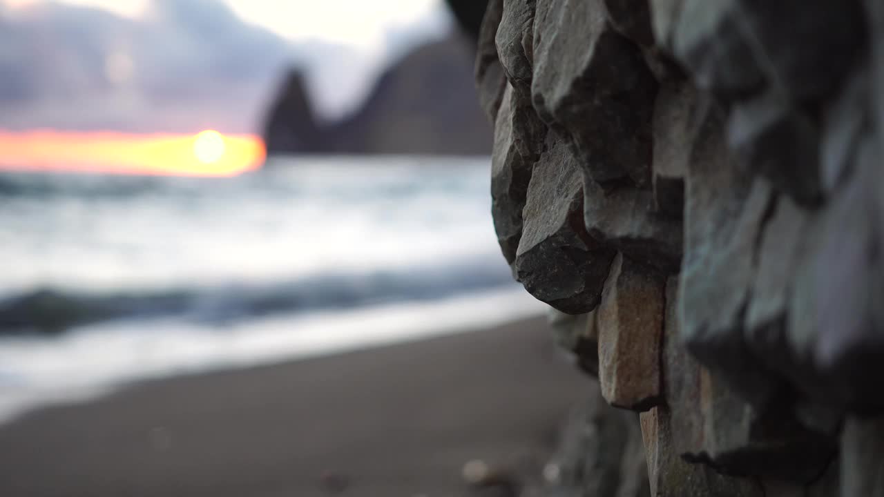 多彩的温暖的日落在海上和火山玄武岩，就像在冰岛。海浪冲击着岩石，在温暖的落日的照耀下，浪花飞溅，浪花翻滚。永恒的自然之美视频素材