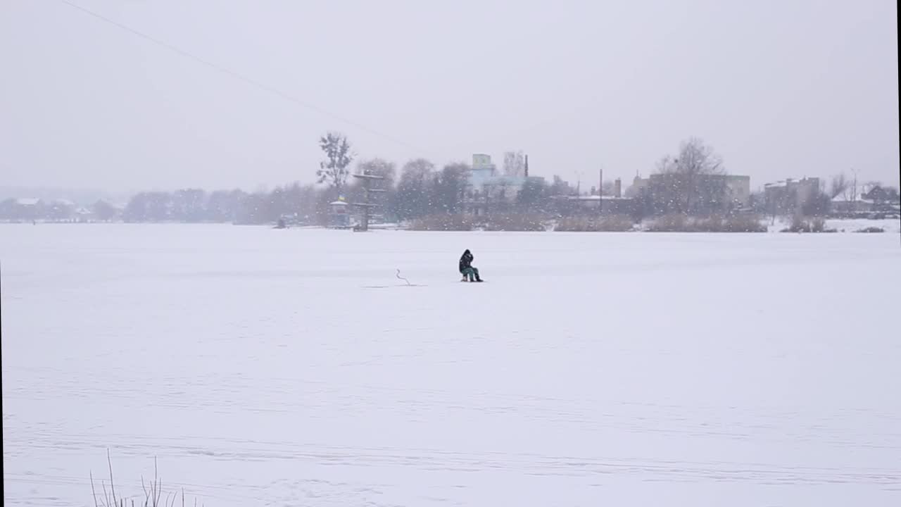 在下雪的时候，和一个渔夫在冰上捕鱼。在恶劣的天气里在湖中央捕捉鲈鱼视频素材