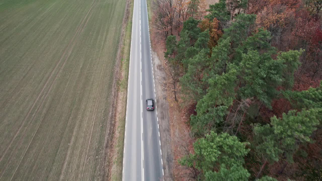 这辆车正行驶在穿过田野的道路上，无人机拍摄了航拍画面。秋天的时候在柏油路上，摄影机跟在车的后面。视频素材