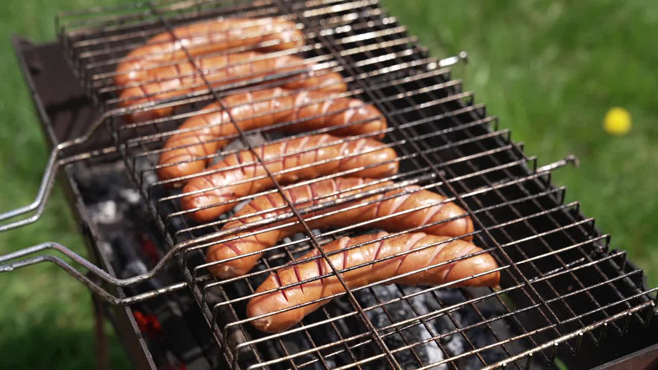 热狗香肠在烟雾中烤着。厨师打开烤架，把多汁的香肠翻过来。夏天野餐的美味食物。吃在自然界中。视频素材