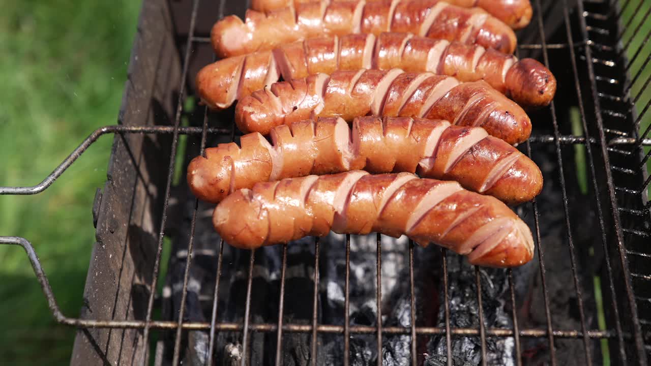 美味的香肠放在烤架上。腊肠在炎炎夏日在烧烤火上烤着。为野餐准备食物。视频素材