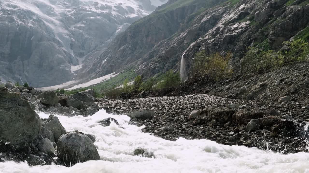 湍急的河流在落基山脉之间流淌，水溅起水花。雪在山上视频素材