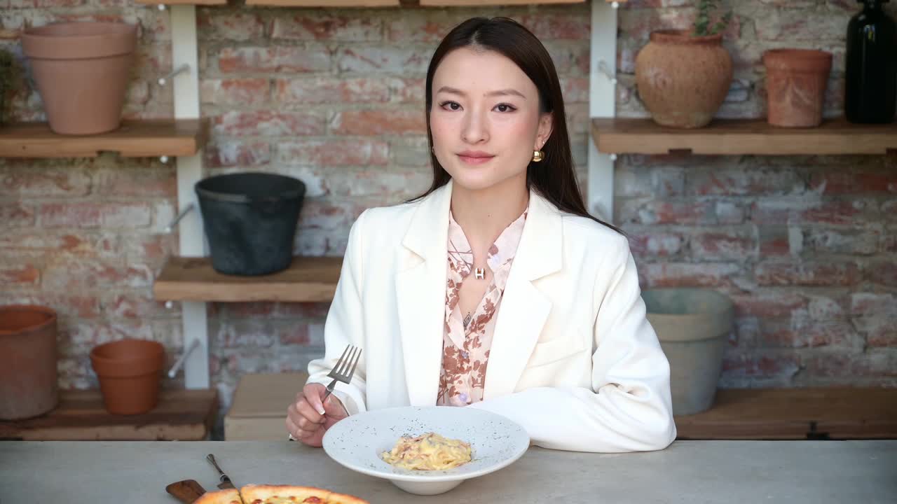 令人惊叹的中国亚洲女人的肖像在餐馆吃意大利面，手里拿着叉子。穿着衬衫的女商人享用午餐或晚餐，老式工业设计的咖啡馆与陶罐视频下载