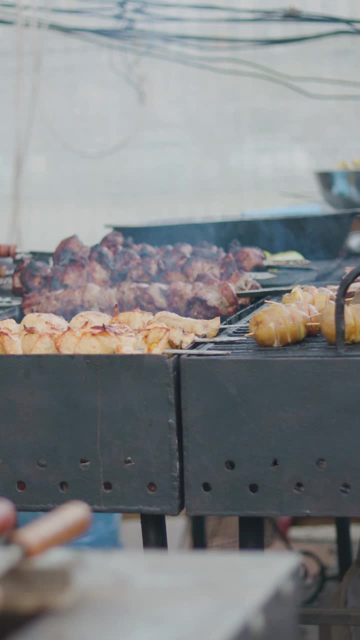 在烤串上翻动土豆。烹饪炸土豆和烤肉串上烤肉。街头食品。垂直视频视频素材