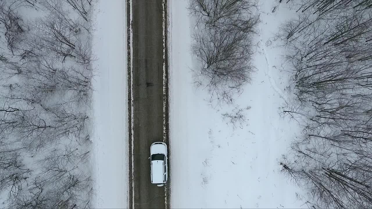 白色的汽车在冬季笔直的道路上行驶，无人机从汽车上方飞过，俯视图。视频素材