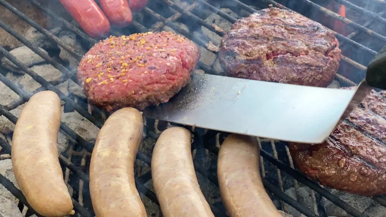 用厨房金属铲烤的汉堡肉饼，小香肠，以及在炭火上烤制的热狗视频素材