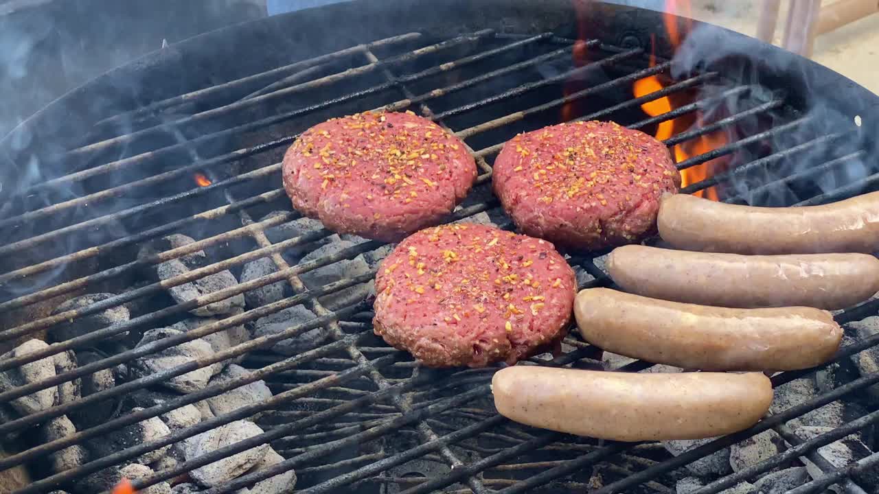 在后院夏季烧烤时，用火钳在炭火上烤热狗、腊肠和调味过的生汉堡视频素材