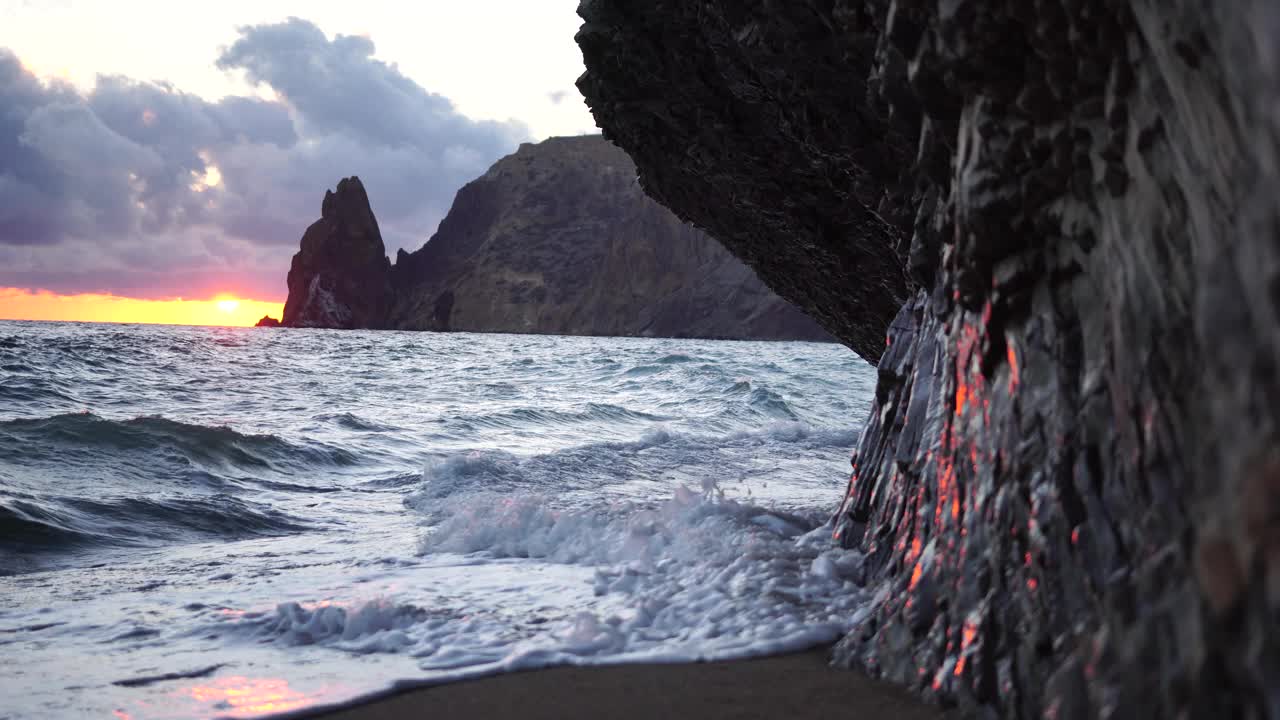 多彩的温暖的日落在海上和火山玄武岩，就像在冰岛。海浪冲击着岩石，在温暖的落日的照耀下，浪花飞溅，浪花翻滚。永恒的自然之美视频素材